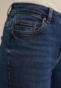 Tmavě modré džíny s přiléhavým střihem, ozdobené oranžovým prošíváním, s několika kapsami a hladkou strukturou.
