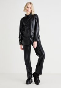 Camisa chaqueta de imitación cuero negro con botones, combinada con pantalones de pierna ancha a juego y zapatos de plataforma gruesos. Textura suave y brillante.
