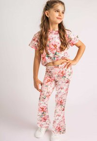 Dwuczęściowy strój w kwiatowy wzór w kolorze różowym, z krótkimi rękawami i spodniami dzwonami, wykonany z miękkiej tkaniny; zestawiony z białymi trampkami.