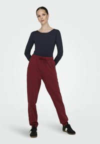 Camiseta de manga larga azul marino con escote redondeado, combinada con pantalones de chándal burdeos que cuentan con cintura ajustable, bolsillos laterales y zapatillas negras.