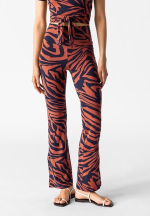 Pantalons évasés et haut assorti en bleu marine avec des rayures de tigre orange. Fabriqué en tissu extensible, avec un nœud à la taille et une coupe ajustée.