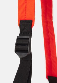 Cinturino arancione brillante con sezioni nere testurizzate. Presenta una fibbia in plastica nera e cuciture rinforzate per la durabilità.