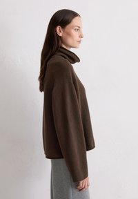 Brązowy sweter z golfem wykonany z miękkiego materiału, charakteryzujący się luźnym krojem, opadającymi ramionami oraz prążkowanymi mankietami, zestawiony z szarym spódnicą.
