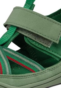 Sandali verdi con parte superiore in pelle scamosciata, cinturino in Velcro regolabile e cinghie intrecciate nei motivi verde, grigio e rosso. Inclusa una soletta testurizzata.