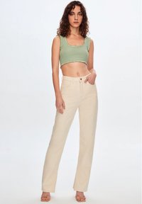 Vaaleanvihreä ohut ribbikuvioinen crop-top, jossa on röyhelöreunat, yhdistettynä korkeavyötäröisiin, kermaisenvärisiin leveälahkeisiin housuihin ja ihonvärisiin sandaaleihin. Yksinkertainen tausta.