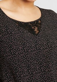 Černý top s výstřihem do V, zdobený růžovými puntíky. Krajkový detail na výstřihu přidává texturu a zajímavost. Měkká tkanina, volný střih.