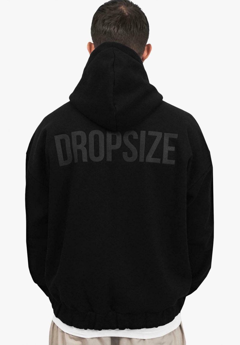 Musta huppari, jossa on suuri "DROPSIZE" -teksti selässä. Farkkuistuva malli, kiristettävä huppu ja ribattu helma. Pehmeä materiaali ja tekstuurinen kangas.