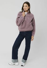 Pull en polaire violet clair avec un col zippé, associé à un jean large bleu marine et des baskets blanches avec des accents gris.