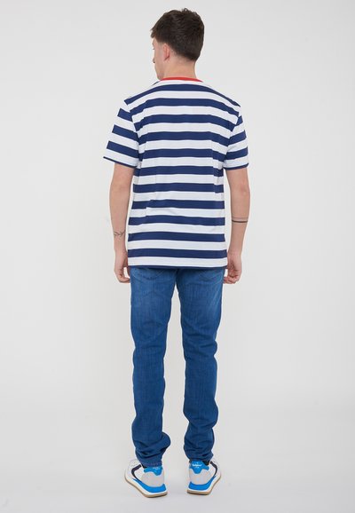 T-shirt a righe blu navy e bianche, con scollatura rossa, indossato con jeans blu e scarpe multicolori. Vista da dietro che mostra il design e la vestibilità.