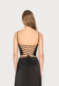 Top corto nero con design allacciato sulla schiena. Realizzato in un tessuto morbido, caratterizzato da spalline sottili regolabili e una silhouette aderente.