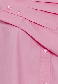 Helles rosa Hemd mit einem Knopfdesign, kleinen, runden Knöpfen, gefältelten Details und einer glatten, leichten Stoffstruktur.