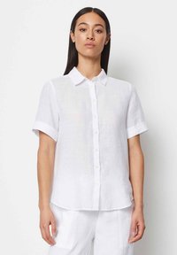 Camicia bianca in lino con maniche corte, chiusura a bottoni e colletto classico. Tessuto morbido, vestibilità rilassata e risvolti alle maniche.