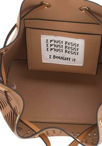 Borsa a secchiello in pelle color tan con motivo a taglio, parte superiore rotonda e bordi neri. All'interno è presente un'etichetta in tessuto con la scritta "DEVO RESISTERE... L'HO COMPRATA."