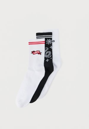 Trois paires de chaussettes montantes : blanches avec des rayures rouges et le logo "Hugo", noires avec un motif de toile d'araignée blanche et des étoiles, et blanches unies.