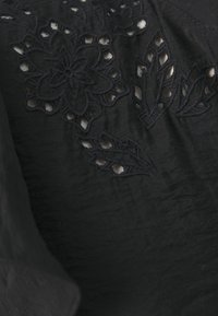 Tessuto nero con ricami floreali e fogliari. I dettagli intagliati sono visibili nel design, evidenziando la texture e l'abilità artigianale.