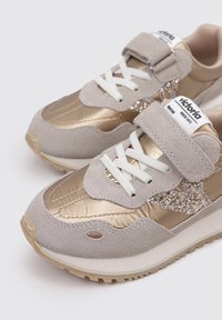 Sneakers beige con accenti dorati, upper in suede e metallic, lacci bianchi e un dettaglio glitterato di lato. Fascia in Velcro per una facile chiusura.