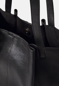 Borsa tote in pelle nera con superficie testurizzata, doppi manici, forma non strutturata e chiusura a scatto interna, rivestita in tessuto liscio.