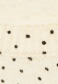 Strickpullover in Off-White mit kleinen schwarzen Punkten. Verfügt über eine gerippte Textur am Saum und einen weichen, flauschigen Stoff.