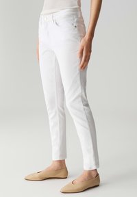 Jeans di denim bianco con un design aderente, cuciture sottili e due tasche frontali. Abbinati a delle ballerine beige senza lacci.