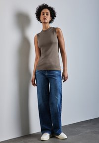 Top senza maniche marrone chiaro, jeans in denim blu larghi e sneakers bianche. Design semplice con una texture liscia e vestibilità rilassata.