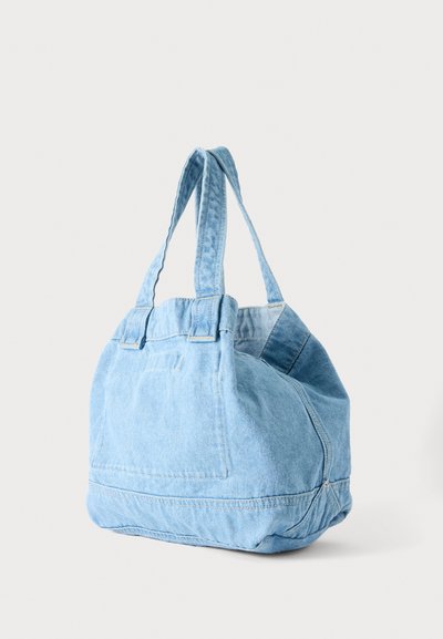 Sac cabas en denim bleu clair avec doubles poignées et coutures visibles, debout sur un fond blanc uni.