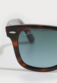 Ochelari de soare tortoise brown cu lentile degrade, cu logo-ul Ray-Ban pe lentilă și accente argintii pe rame.