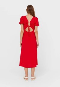 Punainen mekko, jossa on lyhyet puffihihat, avoin selkäosa, joka on kiinnitetty nauhalla, ja keskikokoinen helma. Pehmeä kangas, jossa on sileä pinta.