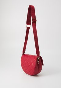 Röd kviltad lädercrossbody-väska med ett tjockt, märkestryckt band och guldfärgad hårdvara. Slät textur och rundad form.