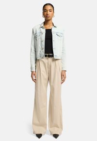 Lyseblå denimjakke med to forlommer, sort tanktop, beige vide bukser og sorte spidse sko. Guld hoop øreringe.