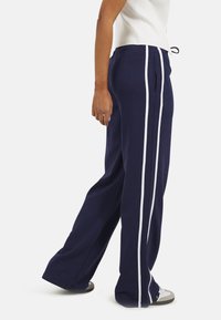 Navyblauwe wijde broek met witte zijstrepen, voorzien van een verstelbare taille en voorzakken, gemaakt van een zachte, lichtgewicht stof.