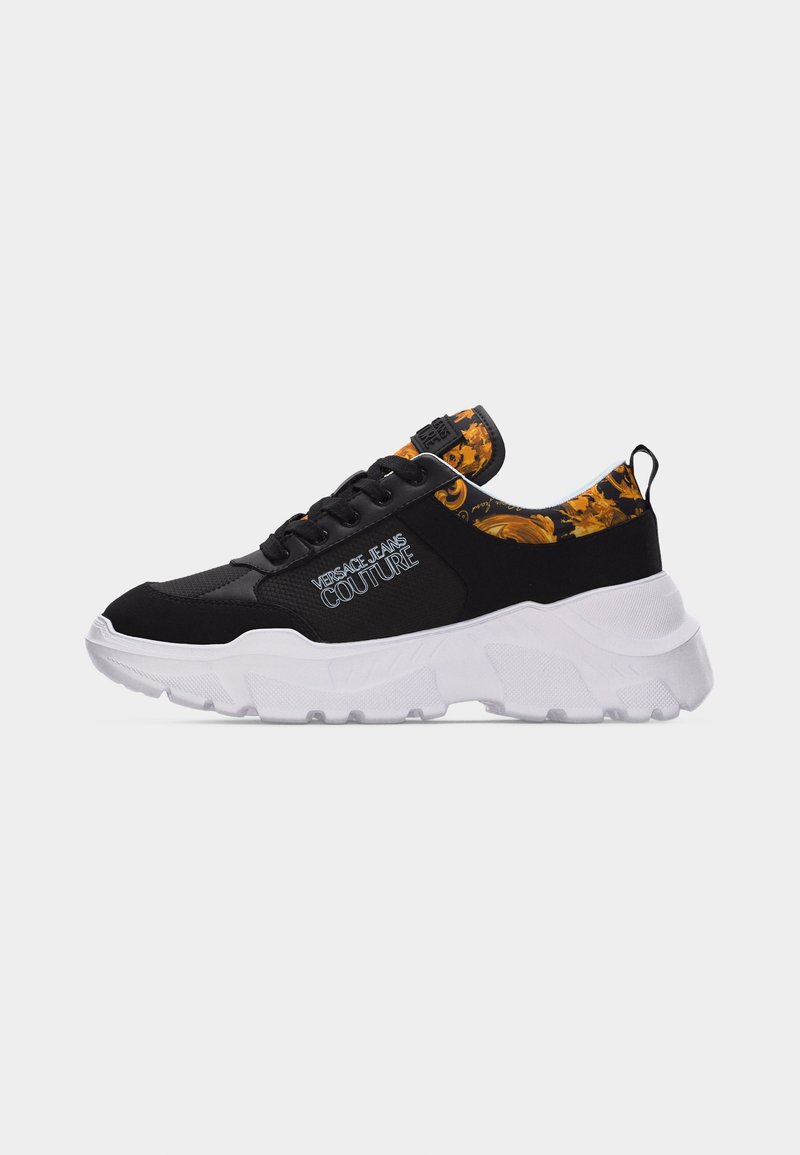 Αθλητικό παπούτσι σε ασπρόμαυρο με χοντρή σόλα, με λογότυπο Versace Jeans Couture και πορτοκαλί εσωτερικό γιακά με σχέδιο λουλουδιών.