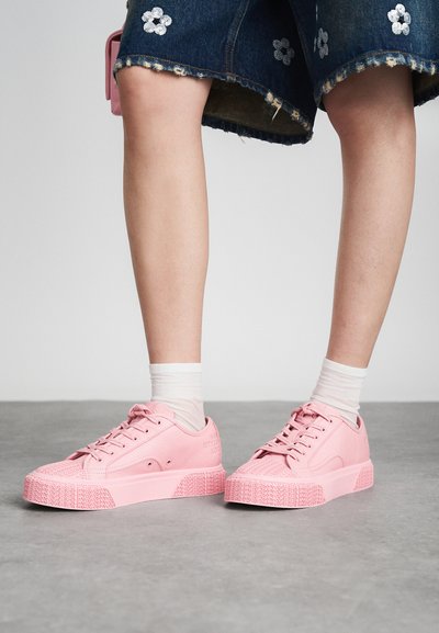 Ružičaste tenisice s teksturiranom površinom, okruglim vrhom i gumenim potplatom imaju uzdignute uzorke. Nošene su uz bijele čarape i traper suknju s cvjetnim detaljima.