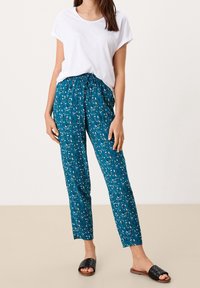 Teal gemusterde broek met een trekkoord in de taille, gecombineerd met een witte t-shirt met korte mouwen en zwarte geweven instappers.