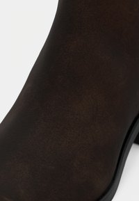 Rjavi semisuvn čevlj z ovalnim nosom in rahlim peto. Rob ima tanek črn gumijast podplat.