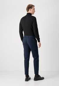 Black turtleneck sweater with long sleeves, paired with navy blue trousers featuring an elastic waistband and back pockets, worn with black shoes.