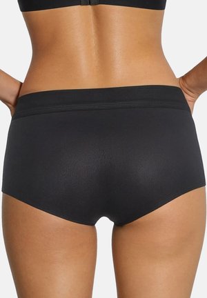Vrouw draagt eenvoudige zwarte naadloze slips met hoge taille en een zwarte beha, weergegeven van achteren met handen op de heupen geplaatst.