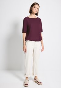 Bordeaux kortærmet bluse parret med cremefarvede bredde benbukser og beige sneakers med maroon og gule striber. Enkelt og afslappet design.