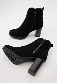 Botas negras de tobillo con un upper de tela texturizada, un zipper lateral y una suela de tacón grueso, que presenta una banda de rodadura resistente para mayor agarre.