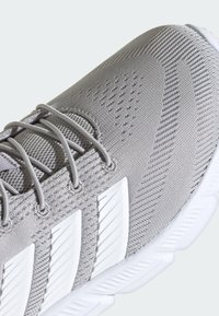 Svetlo šedá športová obuv s vrchom z sieťoviny a štruktúrovanými vzormi, bielymi akcentmi a polstrovanou podrážkou pre podporu.