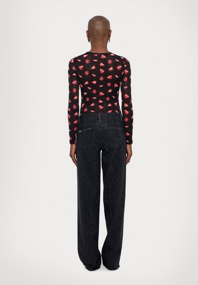 Bodysuit negro de manga larga con estampado de labios rojos; combinado con jeans de mezclilla oscuros de pierna ancha con acentos metálicos de tachuelas.