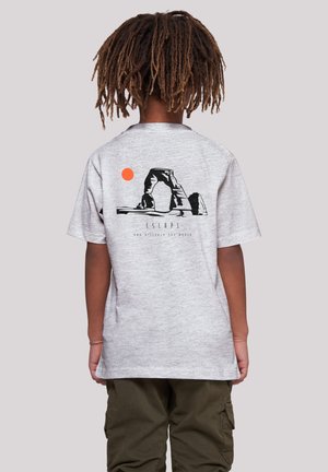Gray cotton t-shirt featuring a black graphic arch design and an orange sun on the back. Short sleeves and relaxed fit, paired with olive cargo pants.