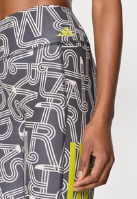 Κολάν με ψηλή μέση, σε μαύρο χρώμα με αφηρημένο άσπρο μοτίβο. Διαθέτει πράσινες λεπτομέρειες, επίπεδες ραφές και εφαρμοστή γραμμή.