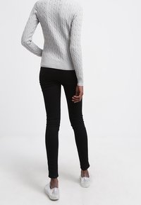 Pull en maille torsadée grise, jean skinny noir et chaussures argentées à enfiler. Motif texturé sur le pull ; tissu lisse du jean.