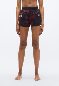 Shorts noirs et rouges à motifs avec une taille à cordon, arborant le logo UFC sur le côté gauche. Le matériau semble léger et sportif.