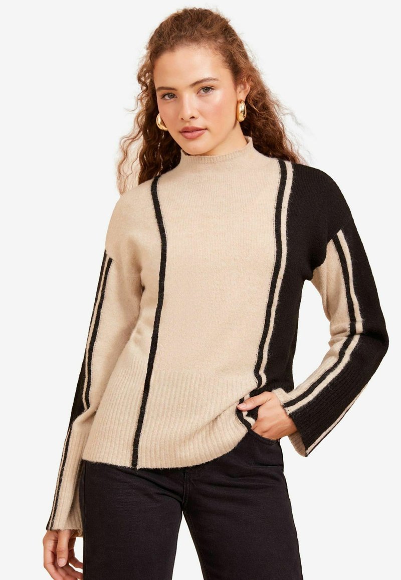Maglione a righe beige e nere con collo alto e texture a coste. Maniche lunghe con righe larghe a contrasto.