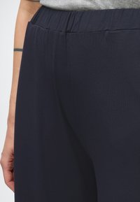 Marinblå vida byxor med elastisk midjeband, tillverkade av mjukt tyg, med en slät textur och ett flödande snitt.