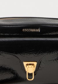 Black patent leather clutch bag with gold hardware. Features logo embossing and a smooth texture, secured with a gold zip closure.