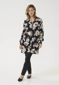 Fekete virágmintás tunika, fehér és barna virágmintákkal, gombos elöl, hosszú ujjaival. Fekete, slim-fit nadrággal és lapos cipőkkel párosítva.