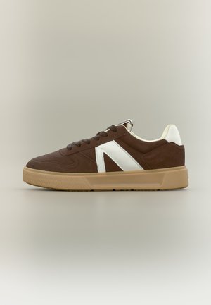 Baskets en daim marron avec accents en cuir blanc, semelle en gomme et fermeture à lacets, montrées en profil latéral sur un fond neutre.