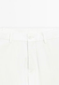 Pantalons en coton blanc avec une taille plate, une fermeture éclair et un bouton. Comprend des passants de ceinture et des poches latérales discrètes. Texture lisse.